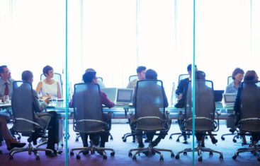 Group of 10 people sitting around a conference table listening to a presentation