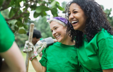 Happy young female environmentalist with friend holding shovel in park