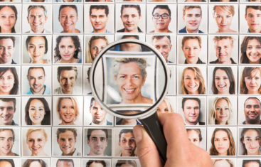 A person holding up a magnify glass to an individual in a sea of images of people